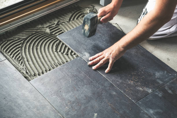 Professional laying dark ceramic floor tiles with adhesive for home renovation and interior flooring installation.